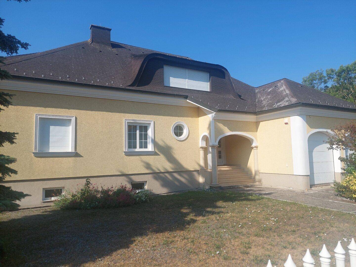 Ansicht der gelben Villa mit Garage, Mansarddach und gepflegtem Vorgarten.