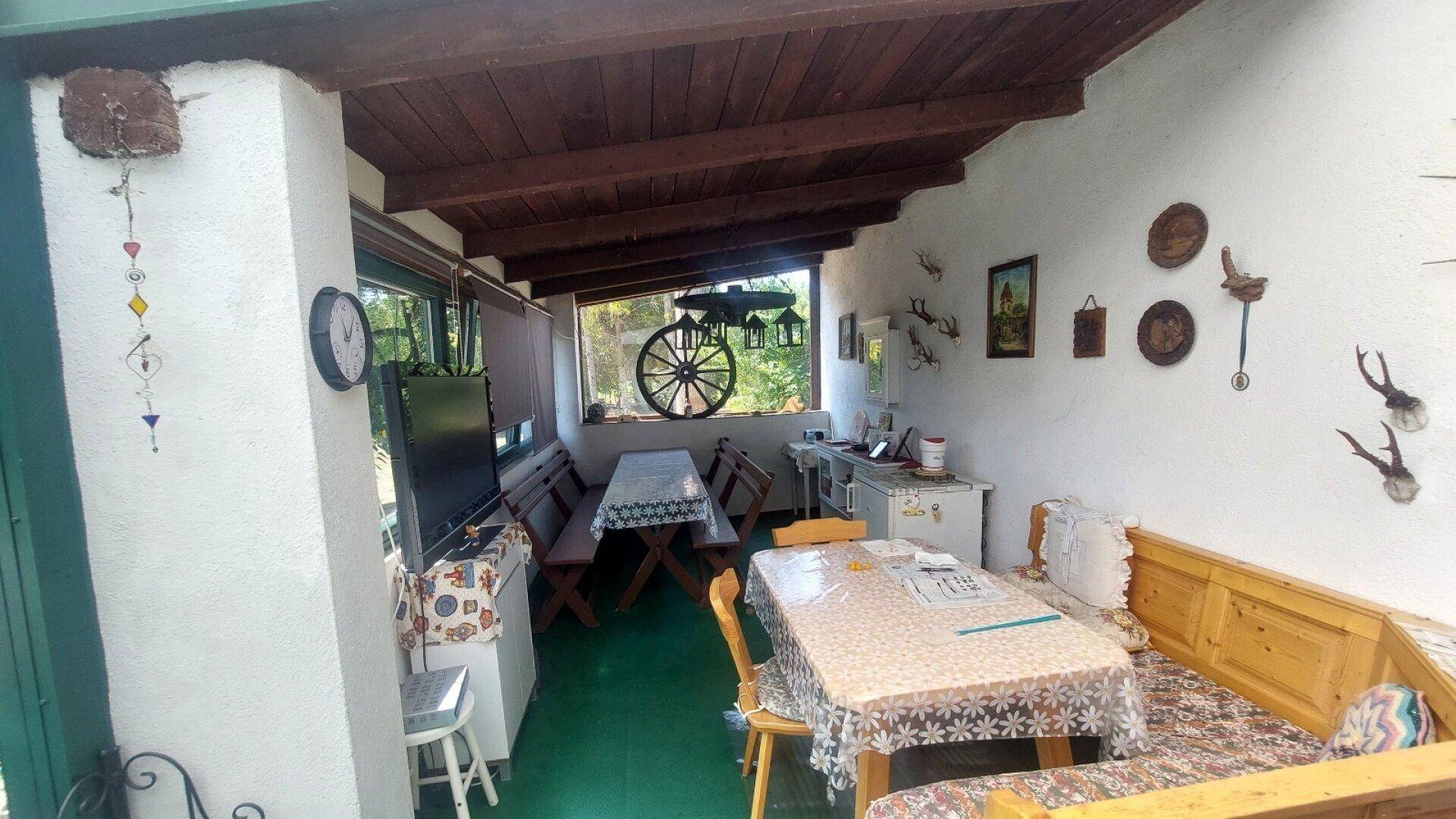 Überdachte Loggia mit Holzbalkendecke, traditionellen Sitzgelegenheiten und Jagdtrophäen.
