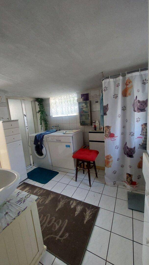 Badezimmer mit Fliesenboden, Waschmaschine und Duschbereich.