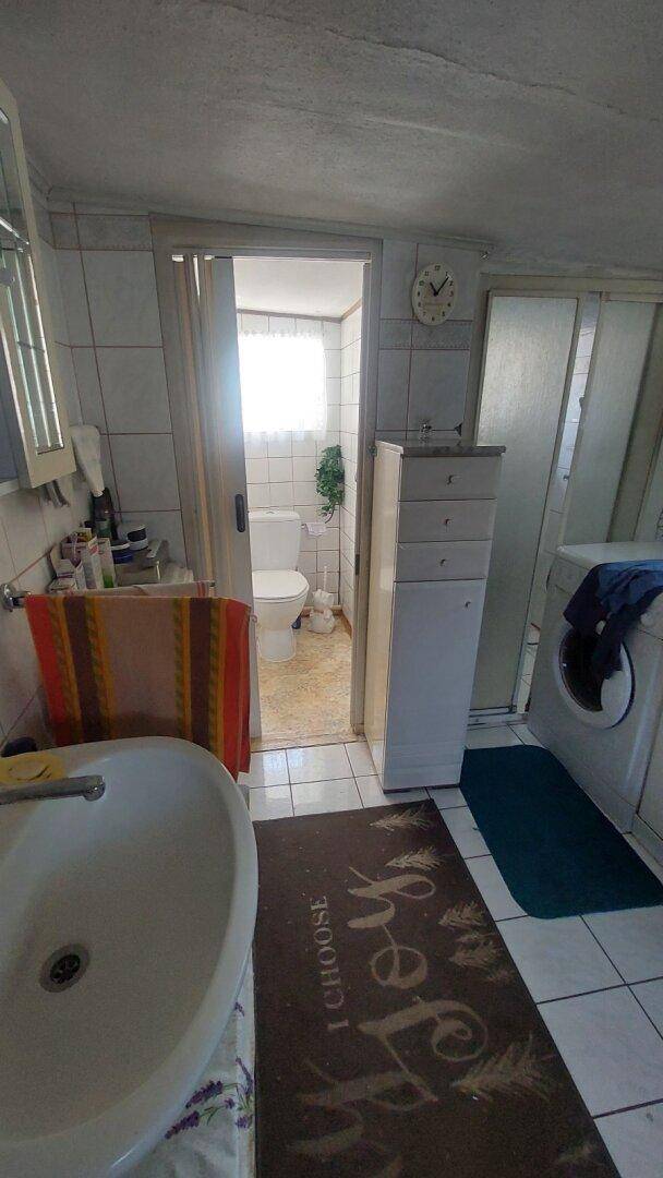 Badezimmer mit Waschbecken, Fliesen und Zugang zu einem separaten WC-Bereich.