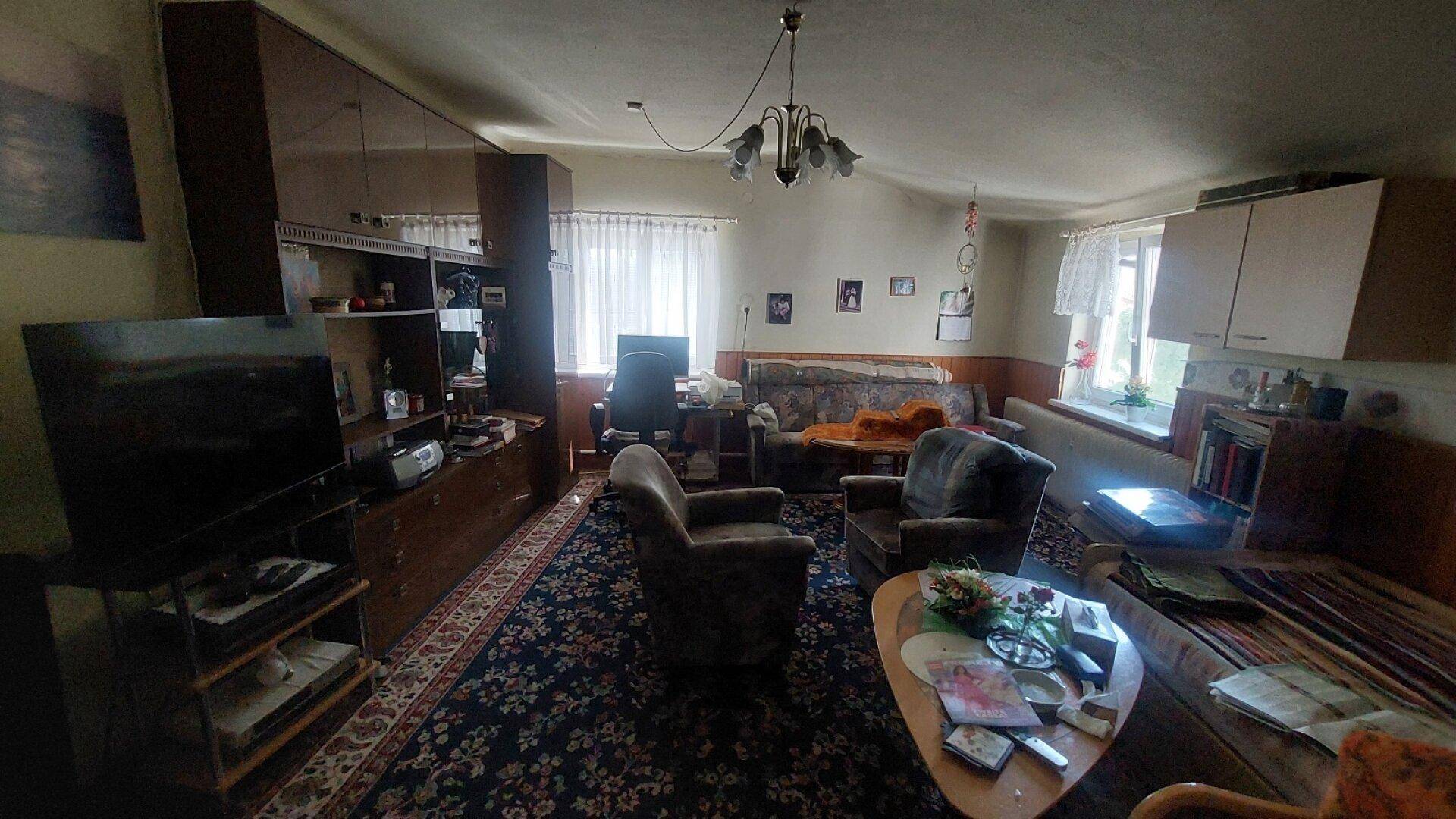 Geräumiges Wohnzimmer mit Teppichboden, traditionellen Möbeln und mehreren Fenstern.