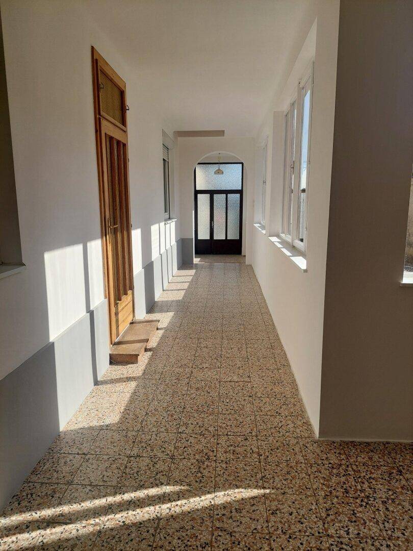 Langer, heller Flur mit Terrazzoboden und Fenstern, die viel Tageslicht hereinlassen.