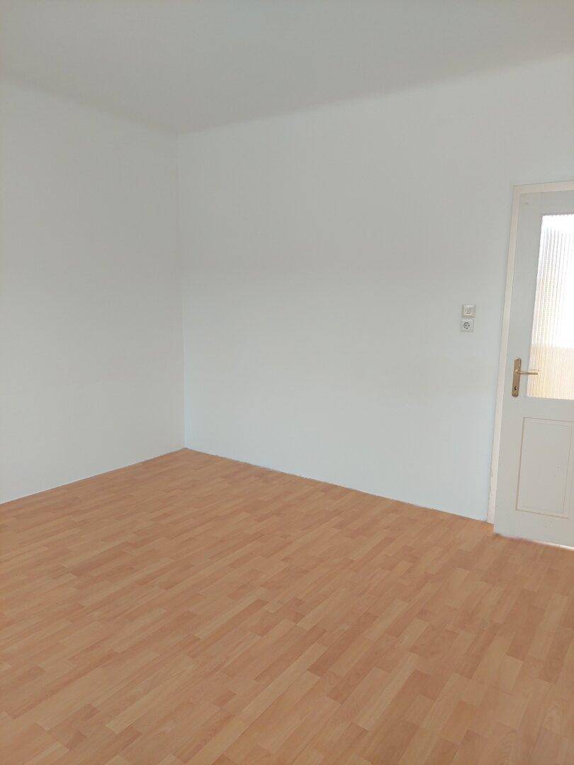 Leeres Zimmer mit hellem Laminatboden und weiß gestrichenen Wänden, bereit zur Einrichtung.