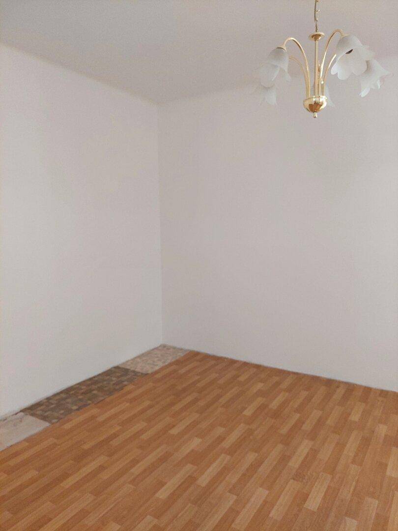 Helles Wohnzimmer mit Parkettboden und klassischer Deckenleuchte, teilweise renoviert.