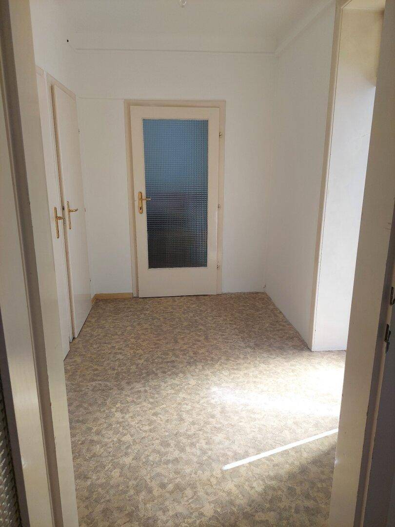 Schmaler Flur mit Linoleumboden und Einbauschränken, der zu einem weiteren Raum führt.