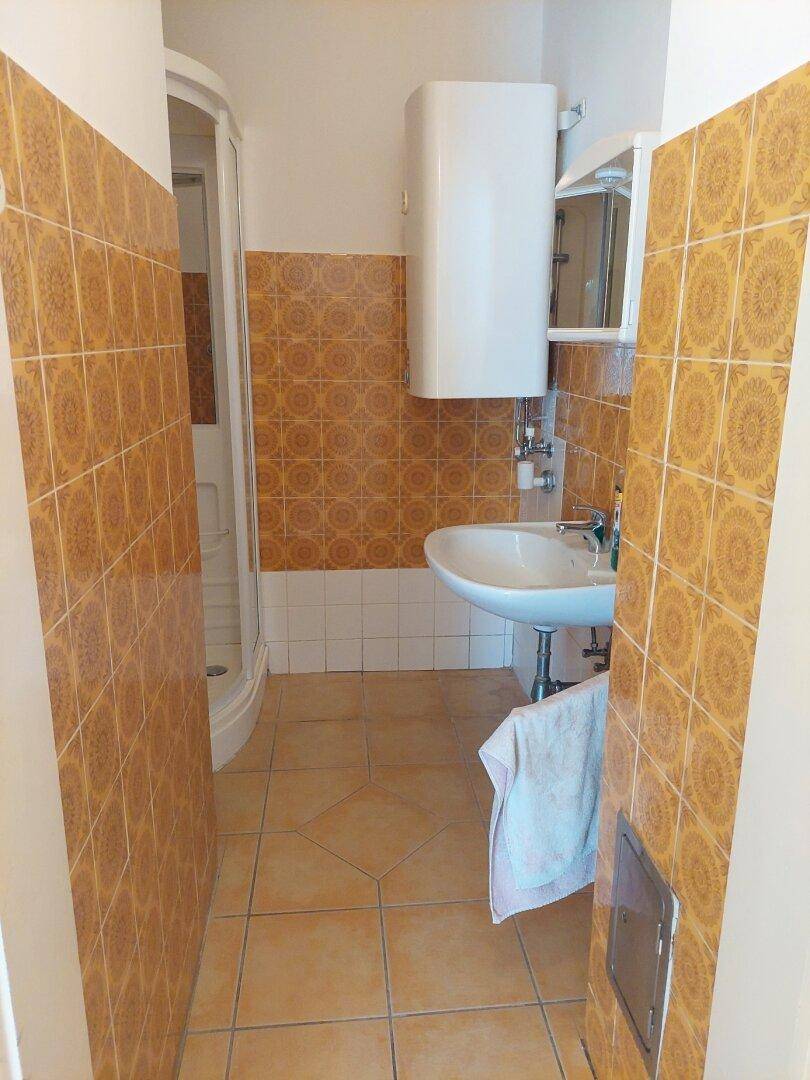 Badezimmer mit gelben Fliesen, Waschbecken und Duschkabine, in gutem Zustand.
