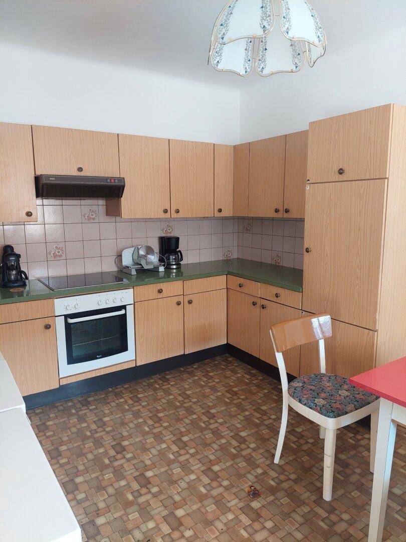 Funktionale Küche mit Holzschränken, grüner Arbeitsplatte und integrierten Geräten.