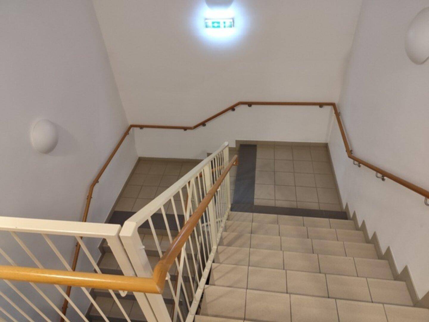 Treppenhaus mit gefliesten Stufen, Handläufen und heller Beleuchtung, führt zu den oberen Etagen.