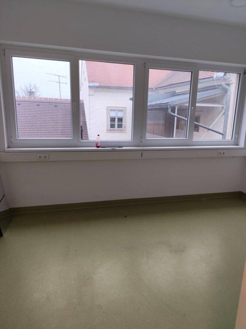 Heller Büroraum mit großen Fenstern, die einen Blick auf die umliegenden Gebäude ermöglichen.
