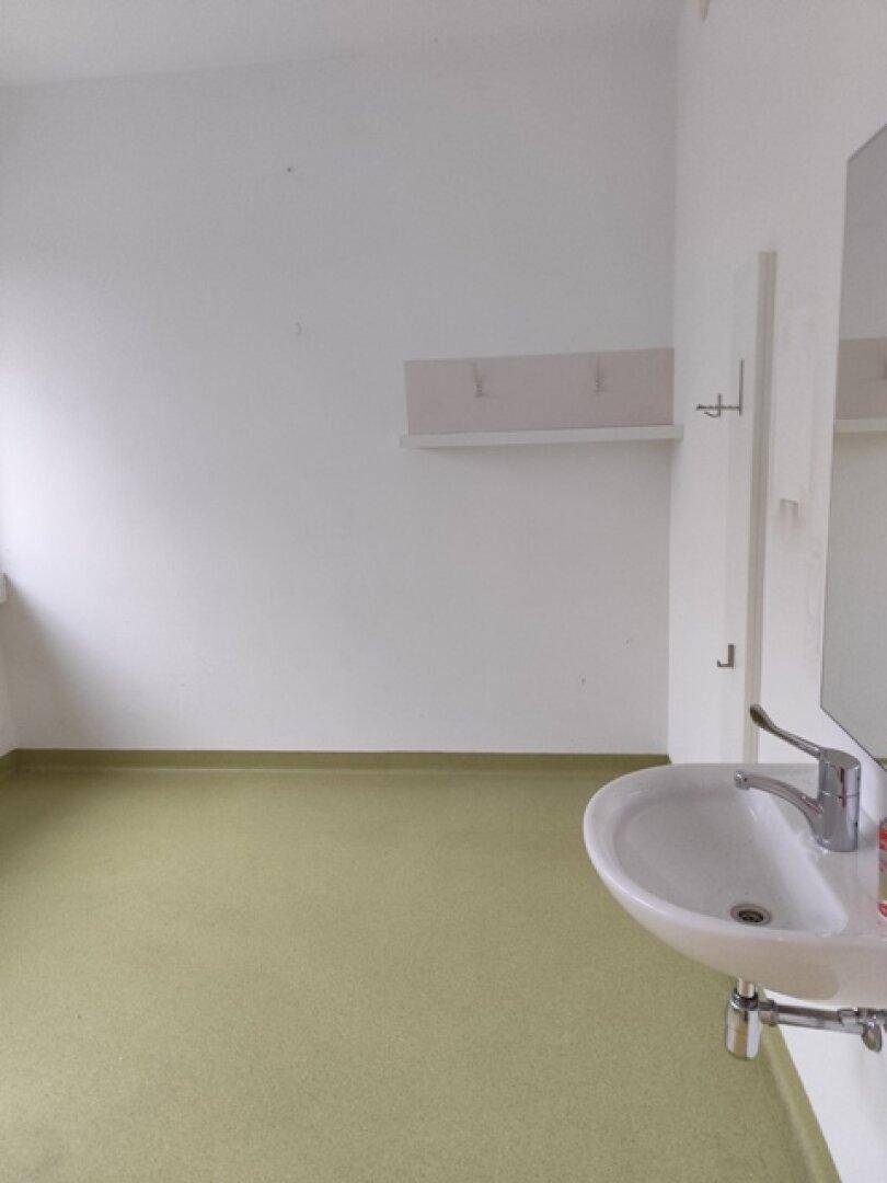 Einfacher Waschraum mit Waschbecken, Spiegel und Garderobenhaken, ideal für Gäste oder Personal.