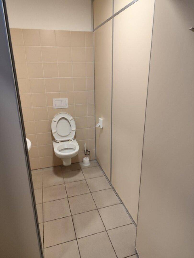 Toilettenkabine mit Wand-WC und beigefarbenen Fliesen, sauber und funktional gestaltet.