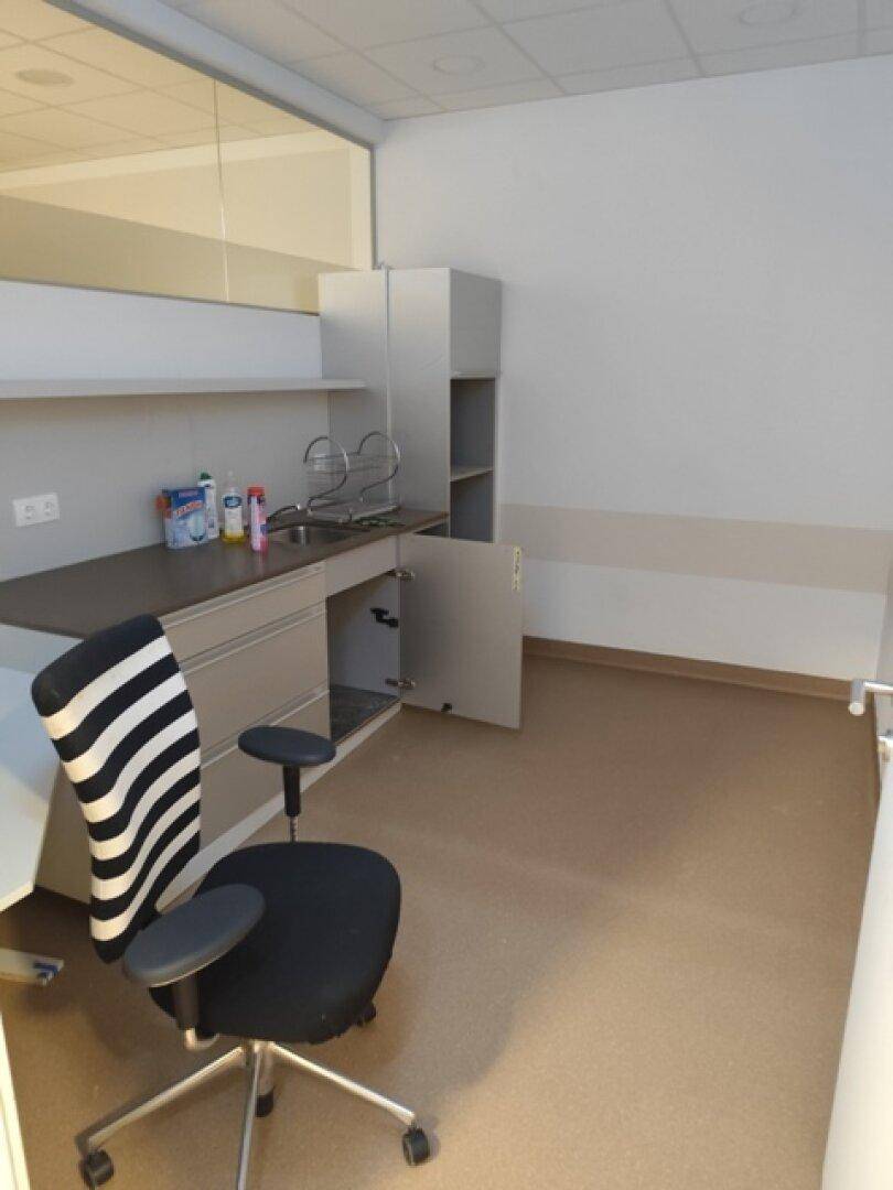 Kleine Küchenzeile mit Spüle, Schränken und Arbeitsfläche, ergänzt durch einen Bürostuhl.