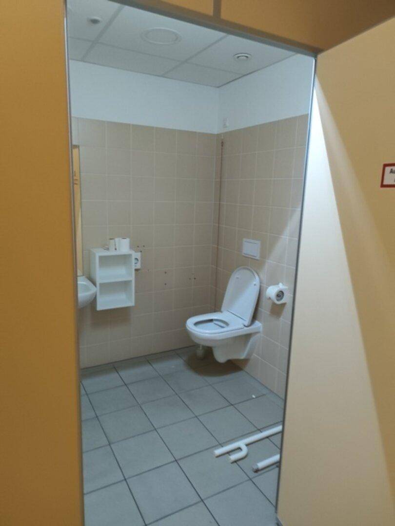 Toilettenraum mit Wand-WC, Waschbecken und beigefarbenen Fliesen, bietet grundlegende Ausstattung.