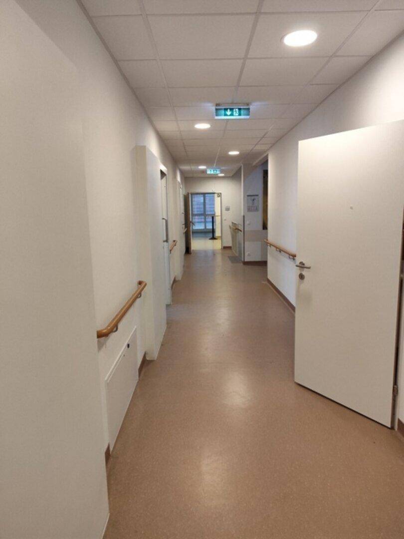 Langer Flur mit Türen zu verschiedenen Räumen, Handläufen und heller Deckenbeleuchtung.