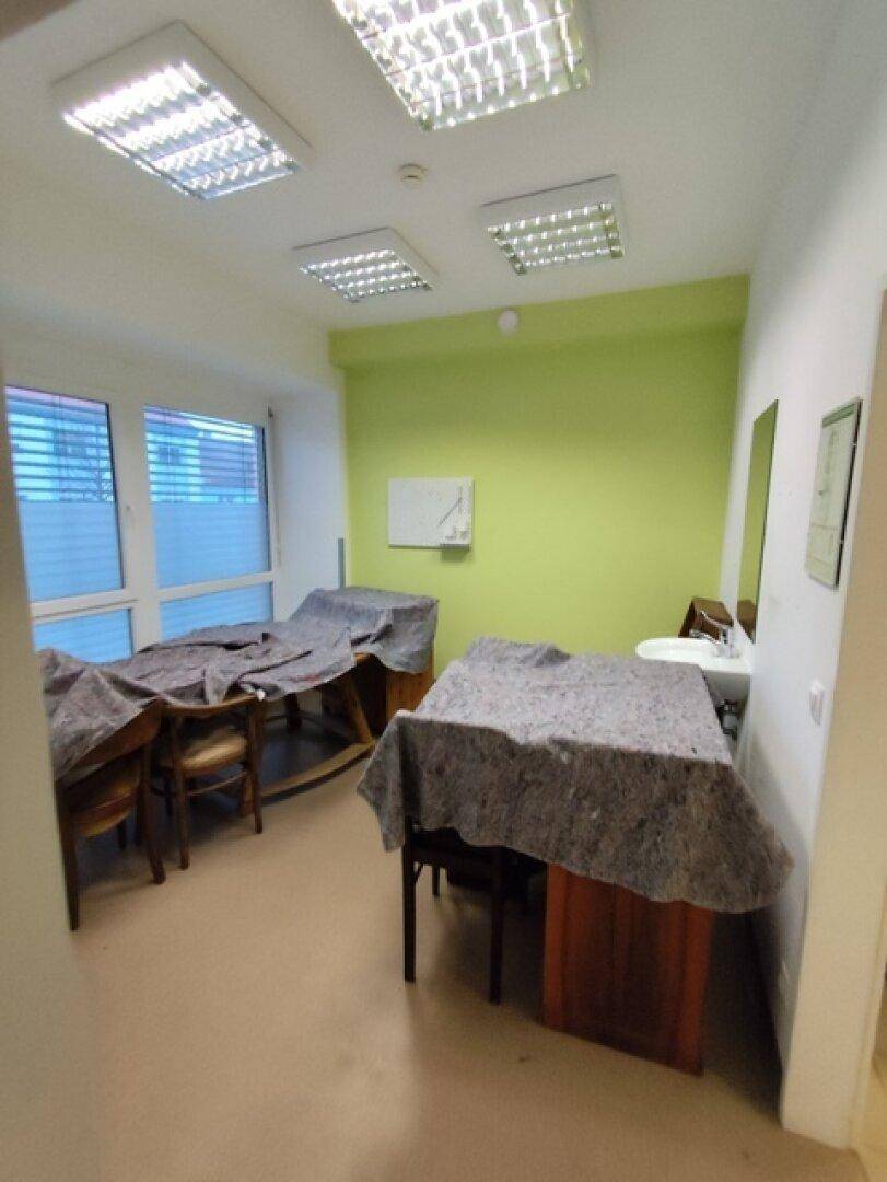 Mehrzweckraum mit auffälliger grüner Wand, Fenstern und abgedeckten Tischen, vielseitig nutzbar.