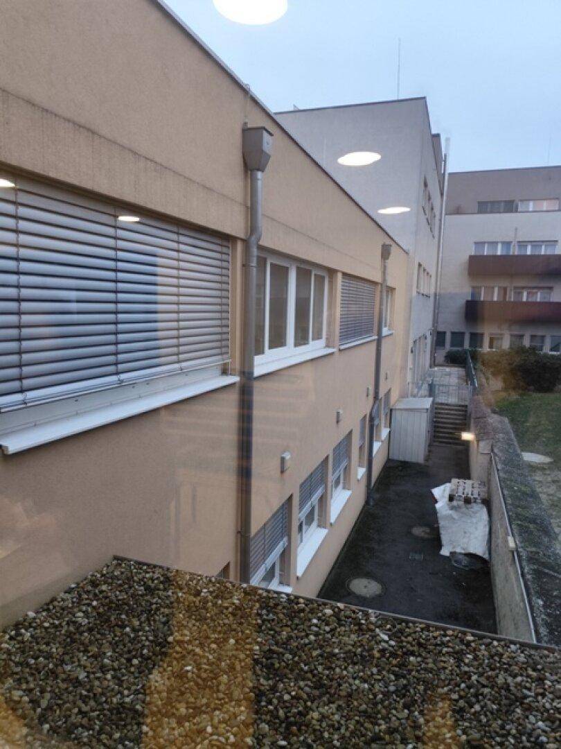 Außenansicht eines Gebäudes mit mehreren Fenstern und Jalousien, umgeben von einer Kiesfläche.