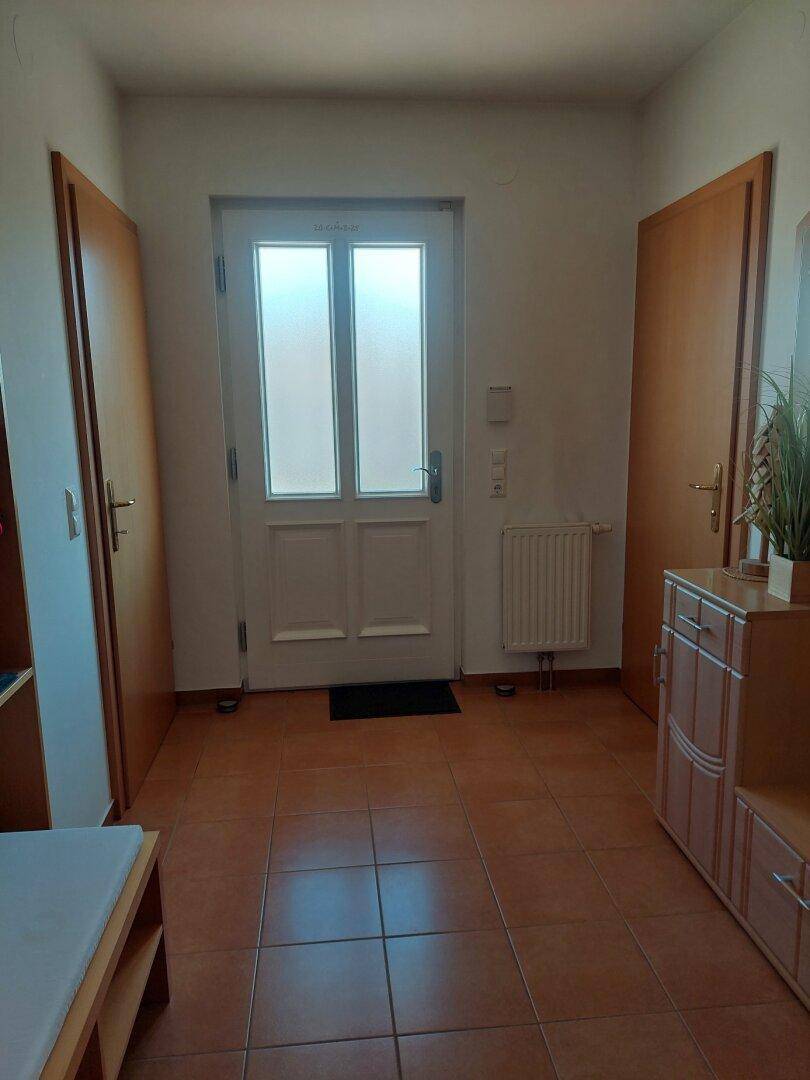 Eingangsbereich mit Terrakotta-Fliesenboden, weißer Haustür mit Glaseinsätzen und Heizkörper.