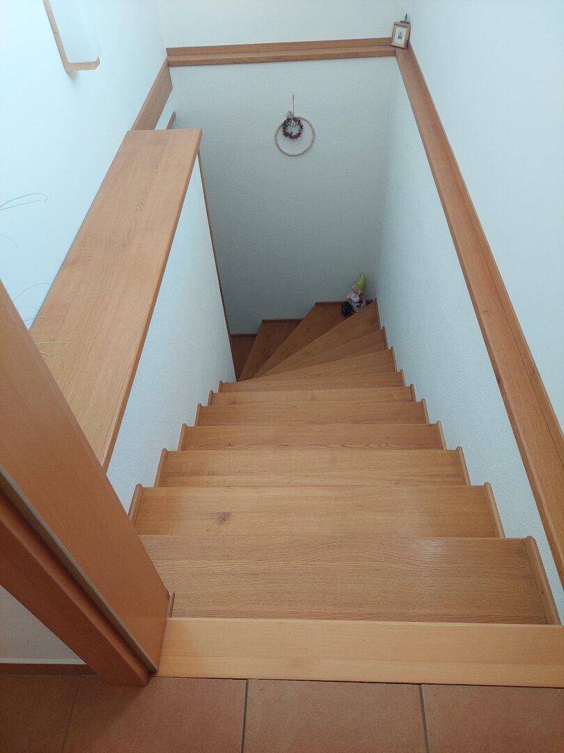 Holztreppe mit hellem Geländer, die in ein unteres Stockwerk führt.