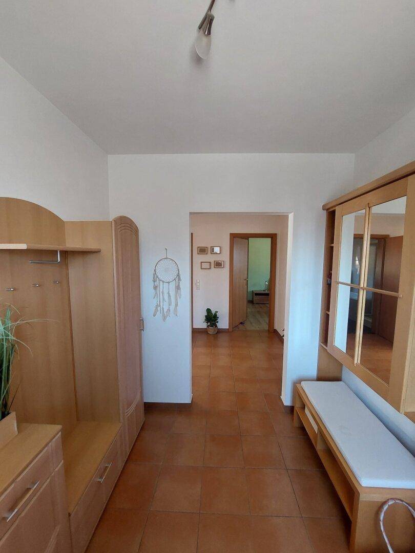 Heller Flur mit Terrakotta-Fliesenboden und Holzmöbeln, der zu weiteren Räumen führt.