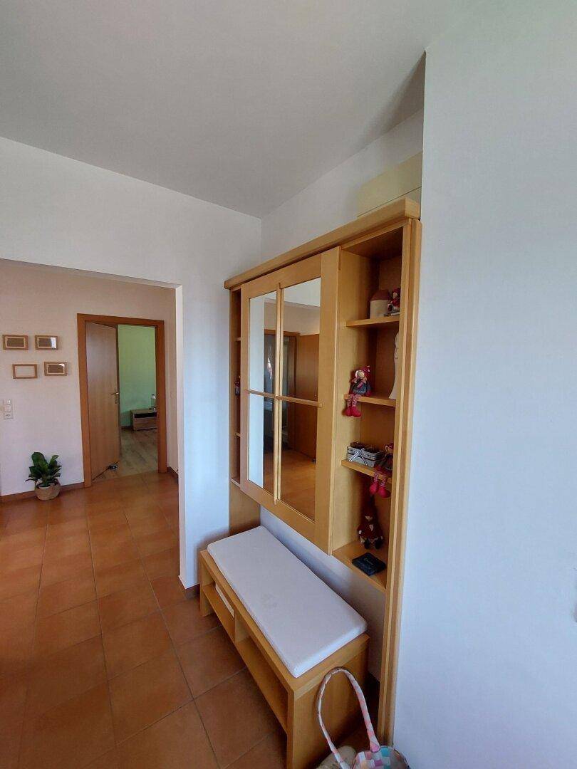 Flur mit Holzschrank, Spiegel und Sitzbank, der einen Blick in angrenzende Räume bietet.