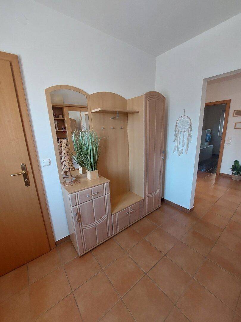 Eingangsbereich mit heller Holzgarderobe, Spiegel und Terrakotta-Fliesenboden.