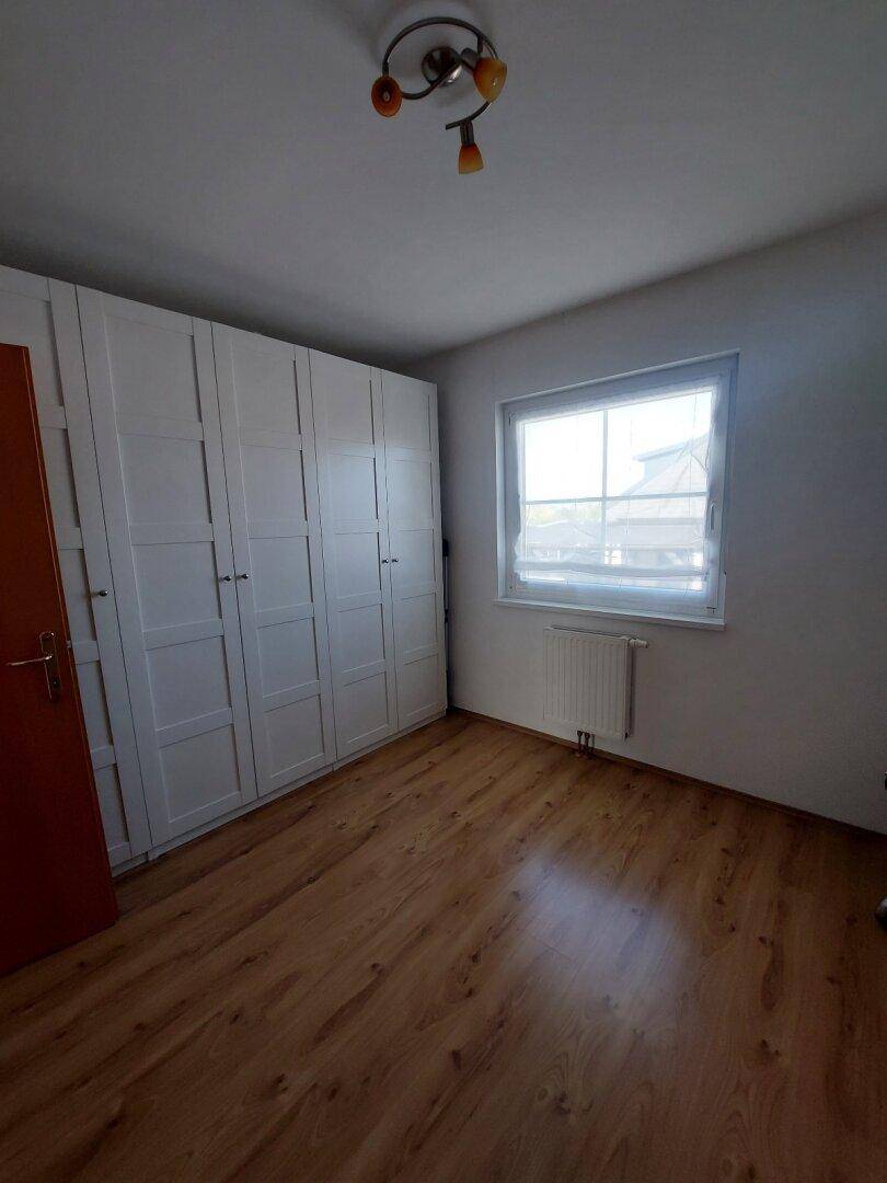 Schlafzimmer mit hellem Laminatboden, großem weißen Kleiderschrank und Fenster.