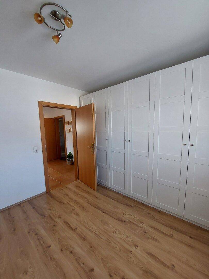 Schlafzimmer mit Laminatboden und weißem Kleiderschrank, der Zugang zu einem anderen Raum bietet.