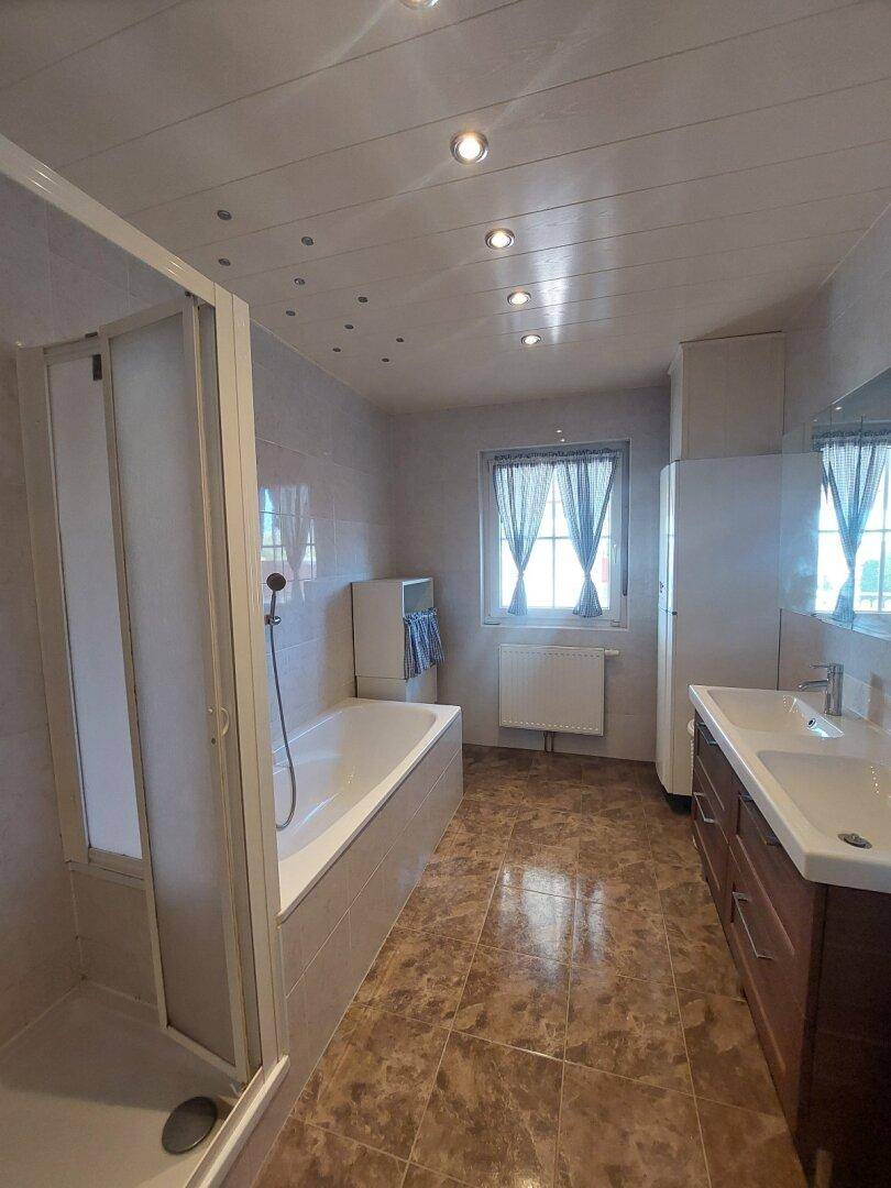 Geräumiges Badezimmer mit Badewanne, Duschkabine, Doppelwaschbecken und Fenster.