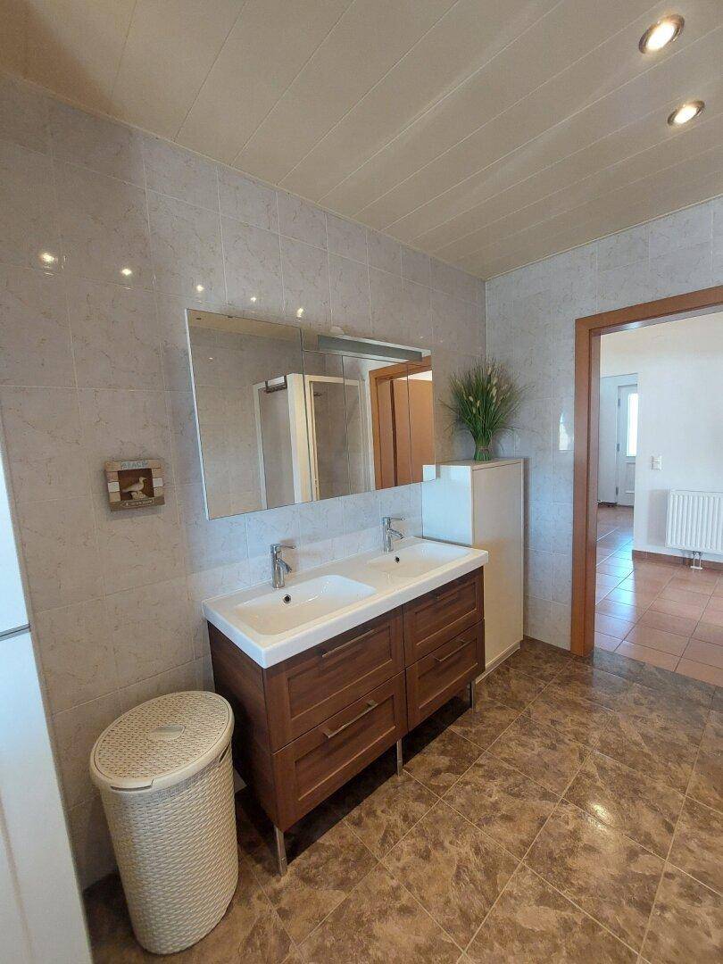 Badezimmer mit Doppelwaschbecken, großem Spiegel und braunen Fliesen, die den Raum elegant wirken lassen.