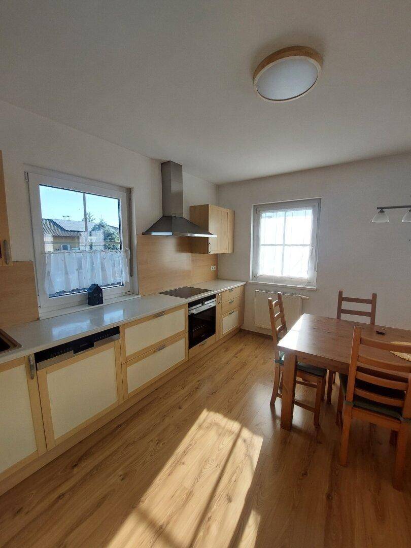 Moderne Küche mit hellen Holzfronten, Laminatboden und viel Tageslicht durch die Fenster.