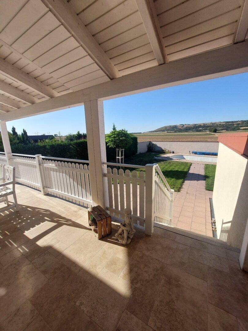 Überdachte Terrasse mit Fliesenboden, weißem Zaun und weitem Blick auf die Landschaft.