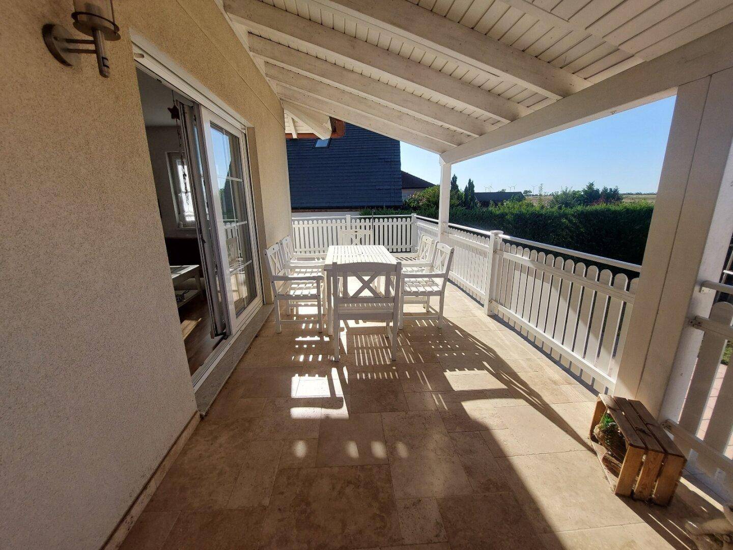 Geräumige überdachte Terrasse mit weißen Gartenmöbeln und Zugang zum Innenbereich.