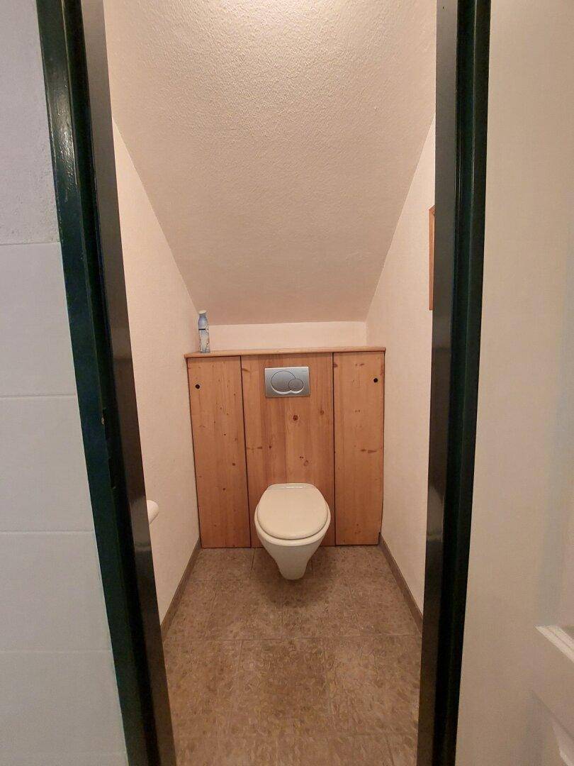 Kleines Gäste-WC mit Holzverkleidung und Wand-WC unter Dachschräge.