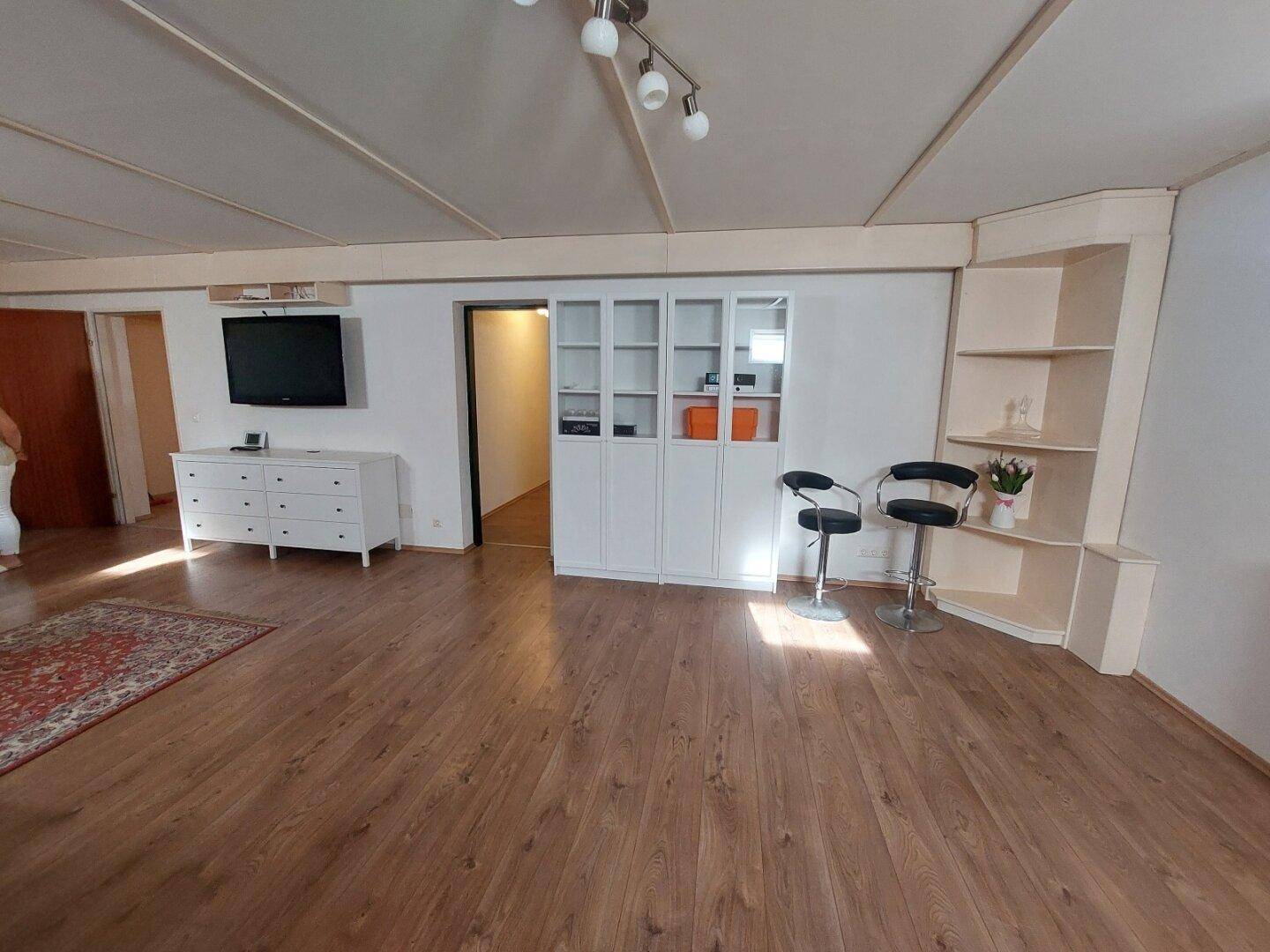 Geräumiger Wohnbereich mit Holzboden, Teppich und integrierten Regalen.