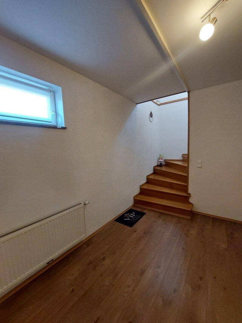 Heller Raum im Untergeschoss mit Holztreppe und kleinem Fenster.