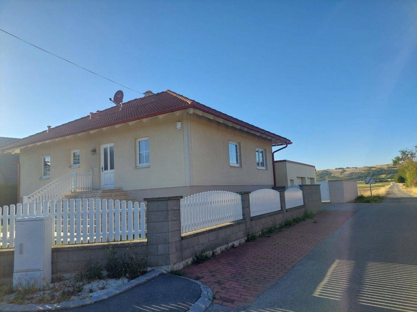 Einfamilienhaus mit Satteldach, weißem Zaun und gepflegtem Vorgarten.