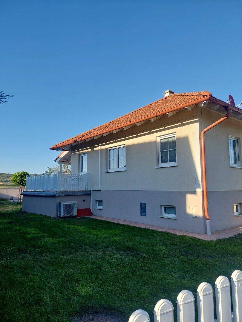 Seitenansicht des Hauses mit Terrasse, grünem Rasen und weitem Blick in die Natur.