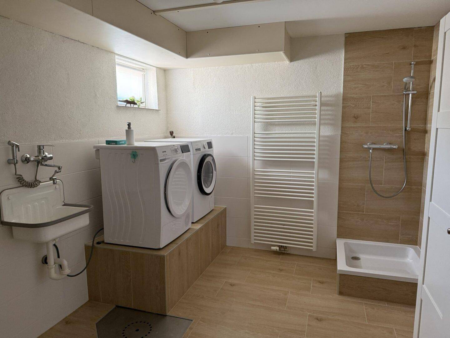 Praktischer Hauswirtschaftsraum mit Waschmaschinen, Dusche und Heizkörper.
