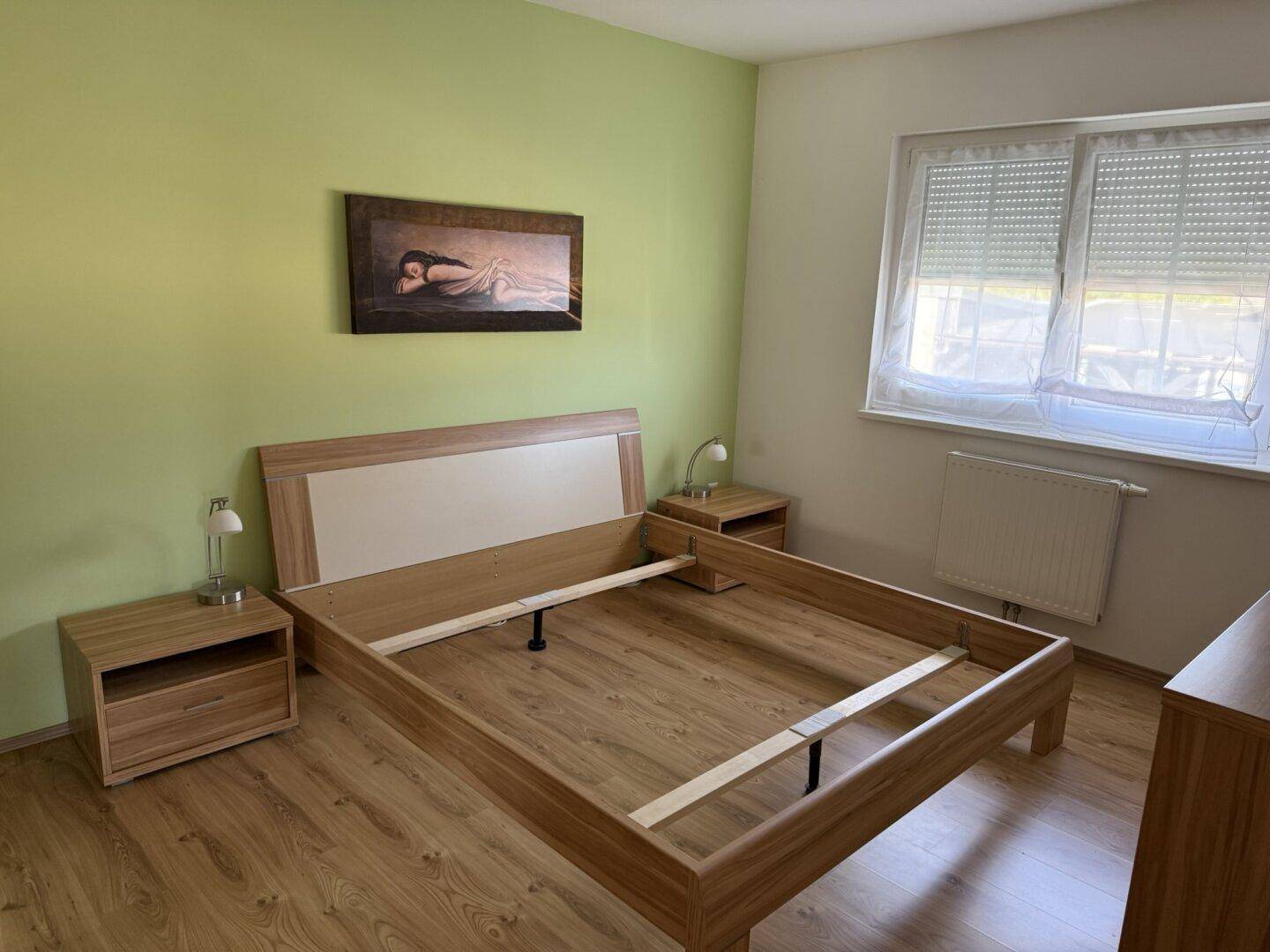 Schlafzimmer mit grün gestrichenen Wänden, Laminatboden und einem Holzbettrahmen.