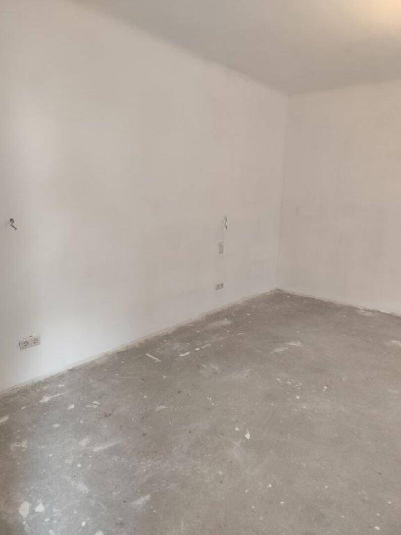 Ecke eines unfertigen Raumes mit weißen Wänden und Betonboden, bereit für den Ausbau.