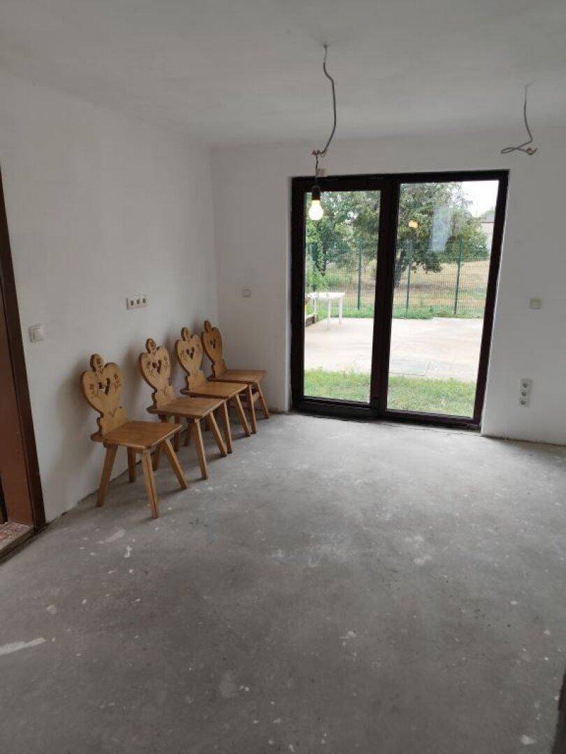 Heller Wohnbereich im Rohbau mit Betonboden, weißen Wänden und Zugang zum Garten.
