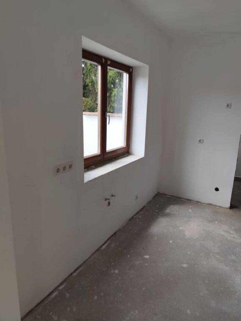 Detailansicht eines Fensters mit braunem Rahmen in einem hellen, unfertigen Raum.