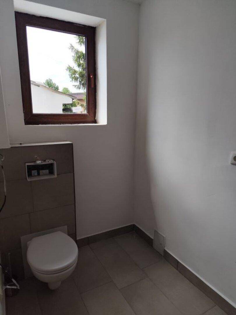 Modernes WC mit wandhängender Toilette, kleinem Fenster und grauen Bodenfliesen.