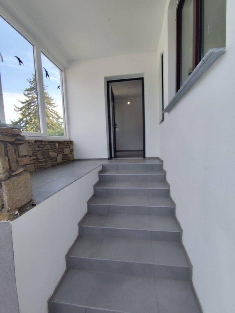 Überdachter Eingangsbereich mit Treppe und großen Fenstern, die viel Licht hereinlassen.