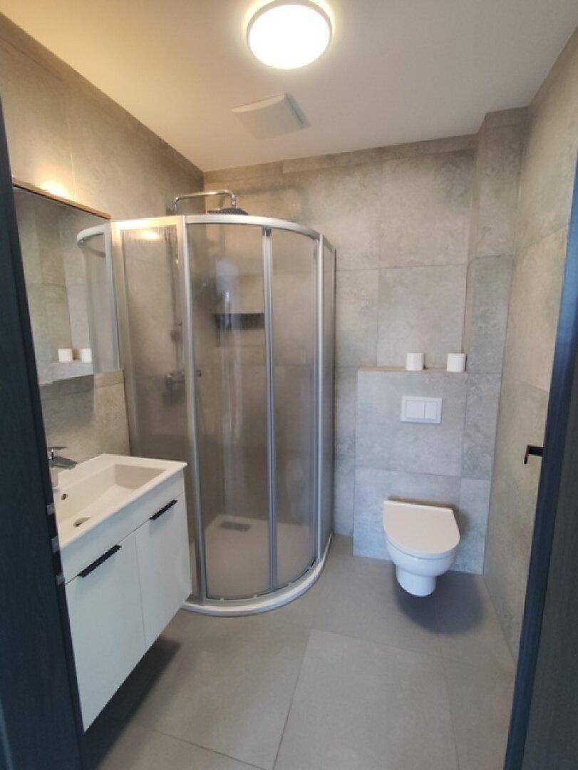 Modernes Badezimmer mit Duschkabine, Wand-WC und grauem Fliesenboden.