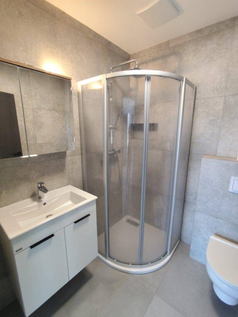 Zeitgemäßes Badezimmer mit Duschkabine, Waschtisch und grauen Wand- und Bodenfliesen.
