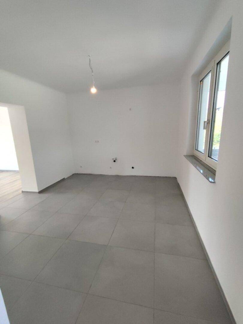 Geräumiger, leerer Raum mit Fliesenboden und Fenster, ideal für eine zukünftige Küche.