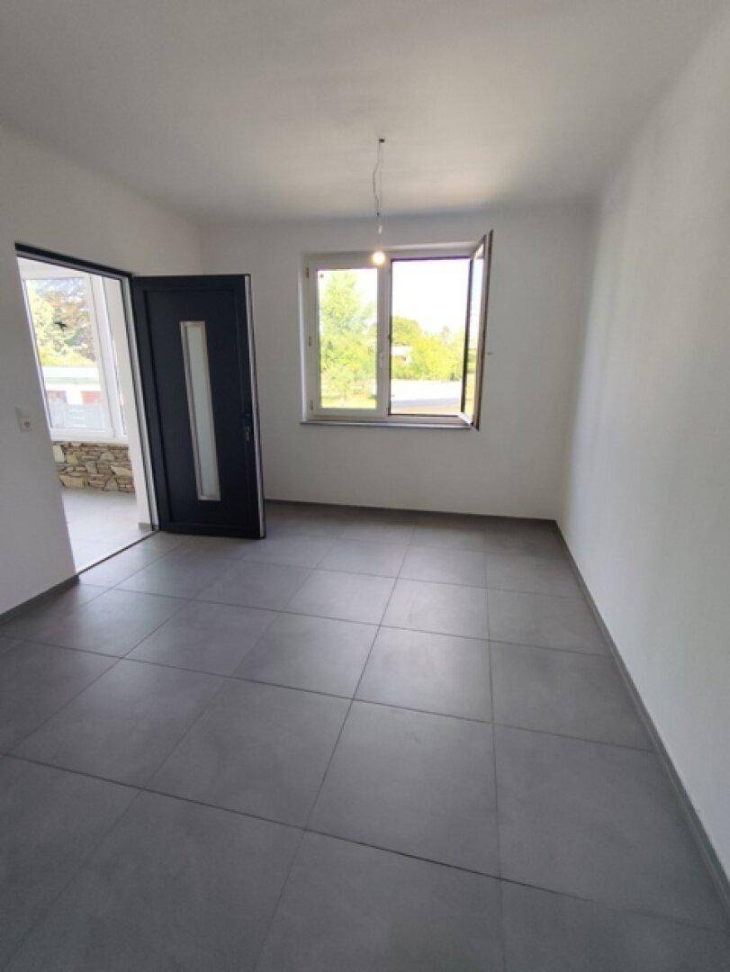 Heller Raum mit Fliesenboden und einem Fenster, das den Blick ins Grüne bietet.