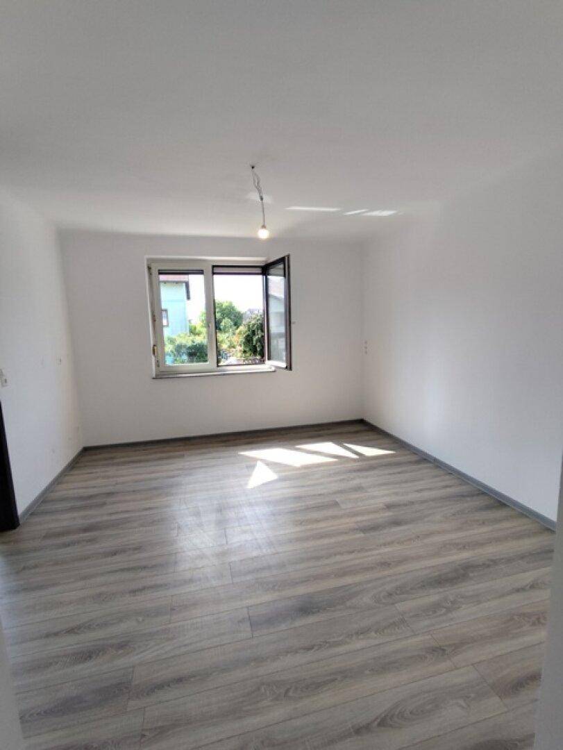 Heller Raum mit modernem Laminatboden und einem Fenster, das Sonnenlicht einfängt.