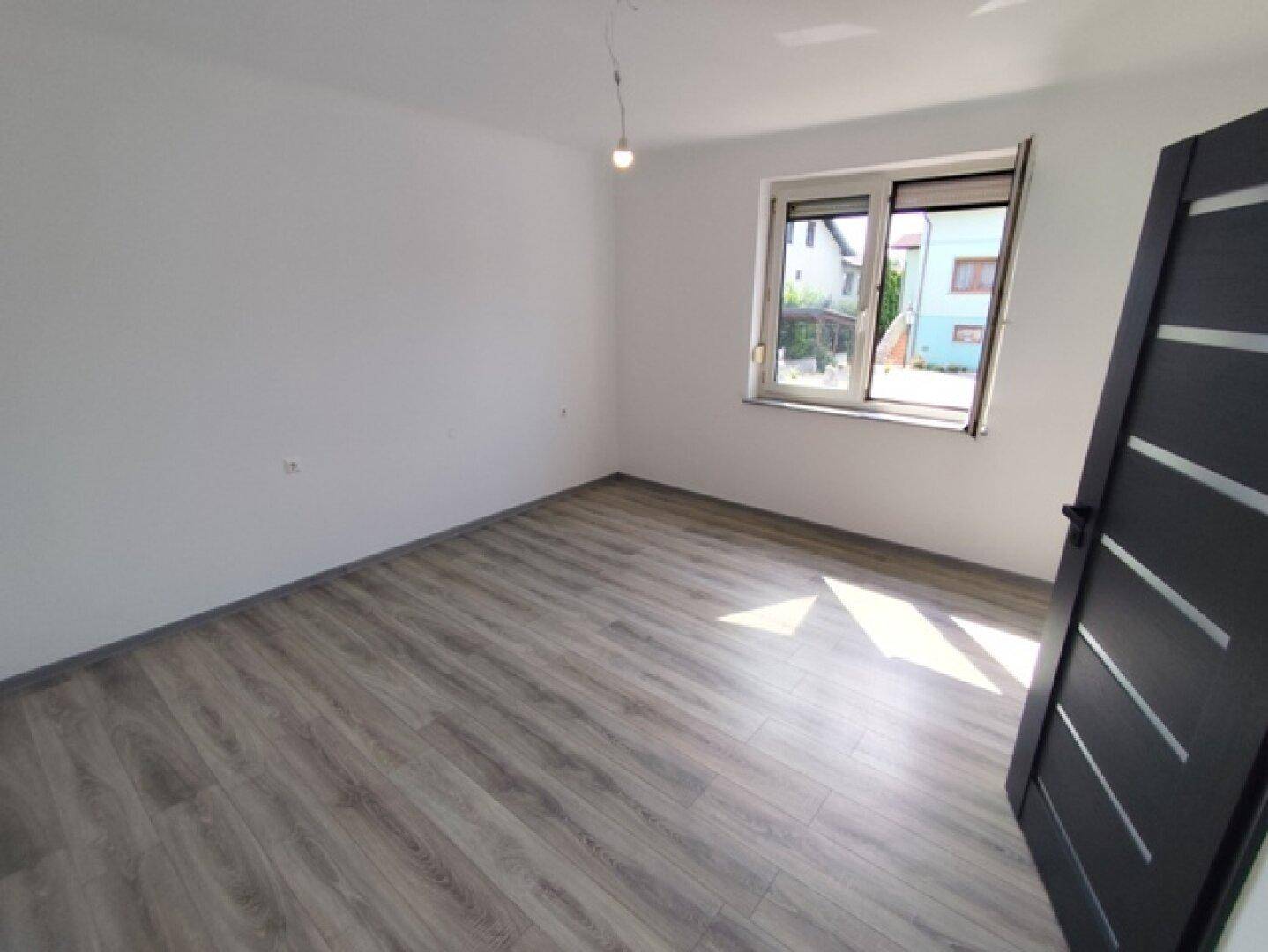 Leerer Raum mit Laminatboden und Fenster, das für eine angenehme Helligkeit sorgt.